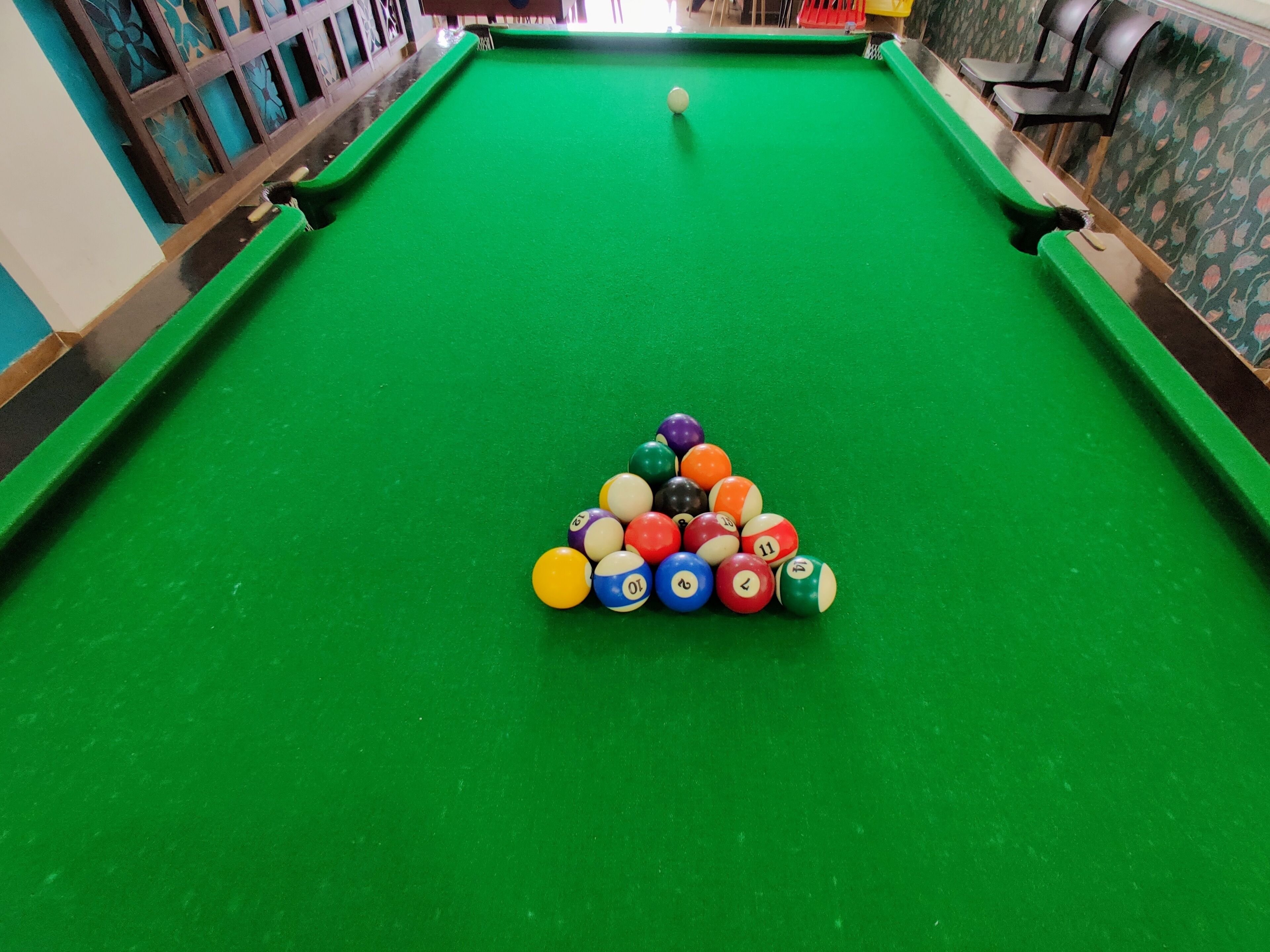 A pool table with a triangular arrangement of billiard balls and a cue ball in the center.
