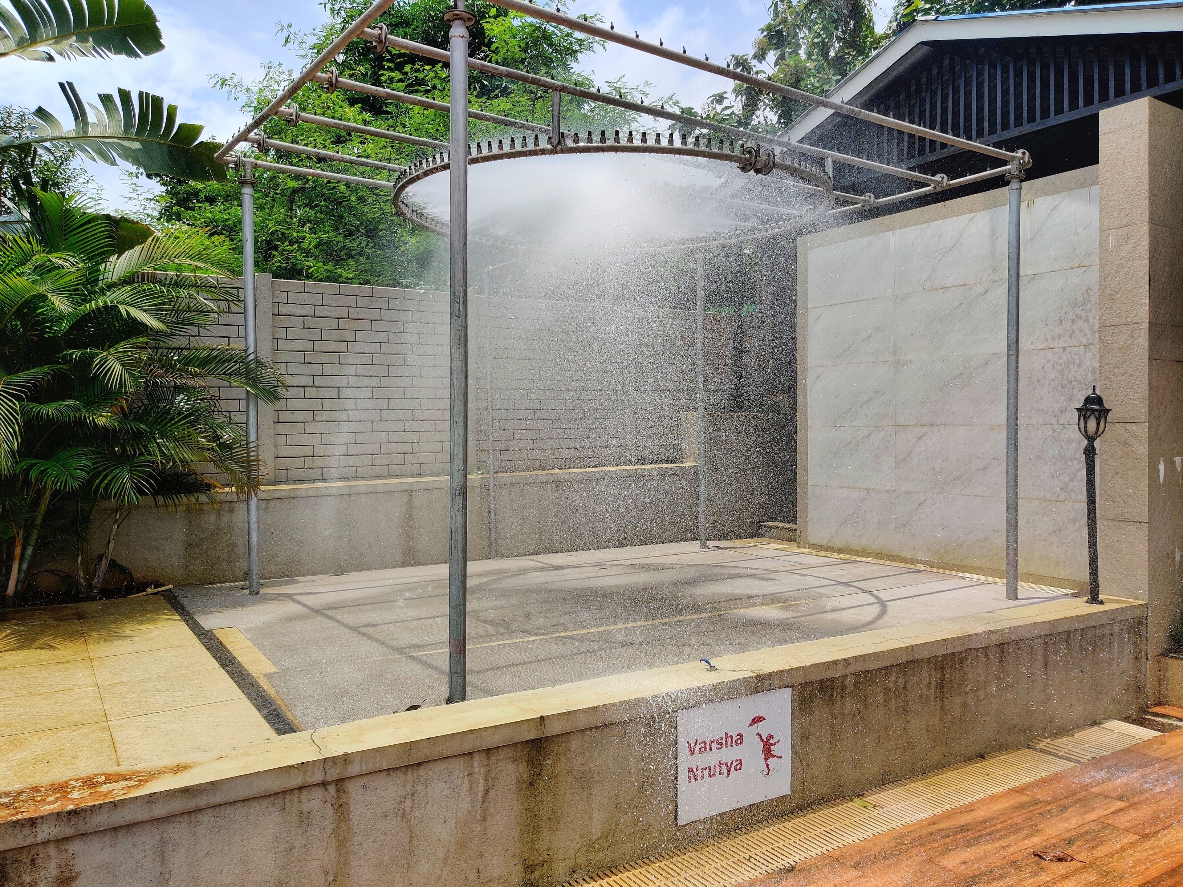 A covered outdoor shower area with a sign reading "Varsha Nrutya".