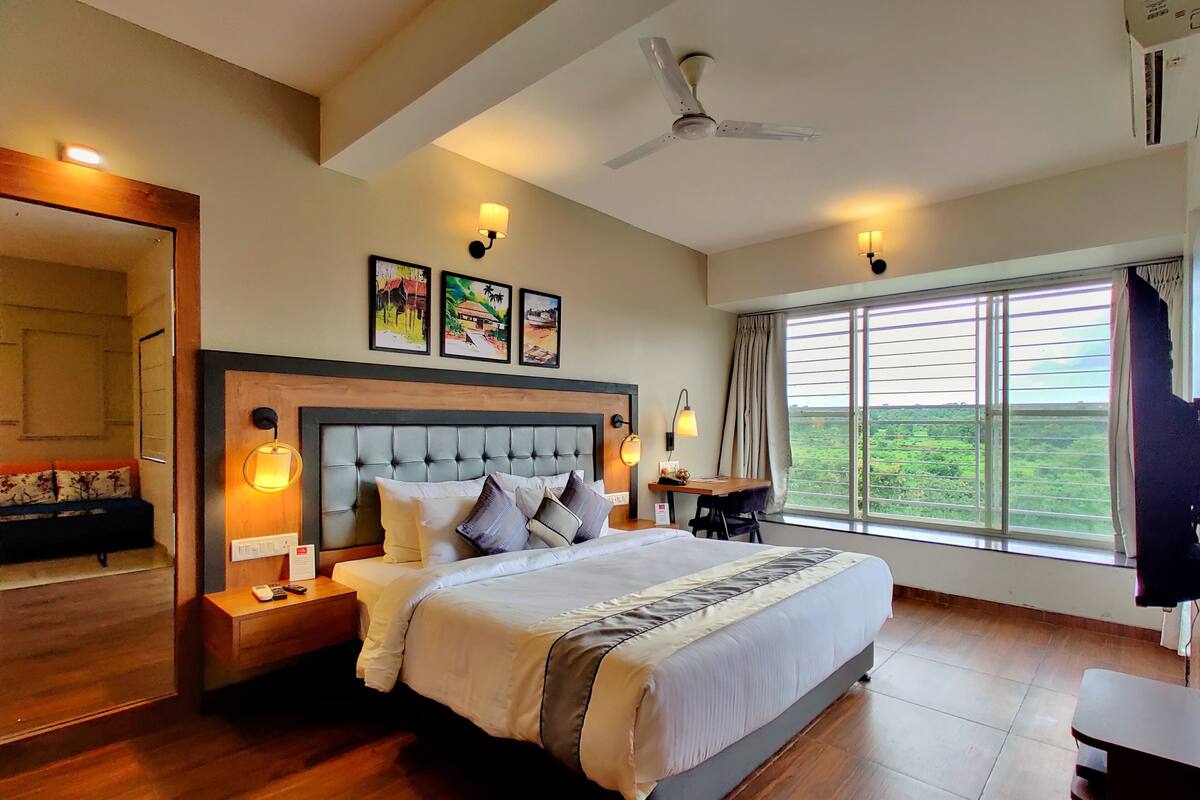 Un dormitorio amplio con una cama grande, un ventilador de techo y vistas a un paisaje verde por la ventana.