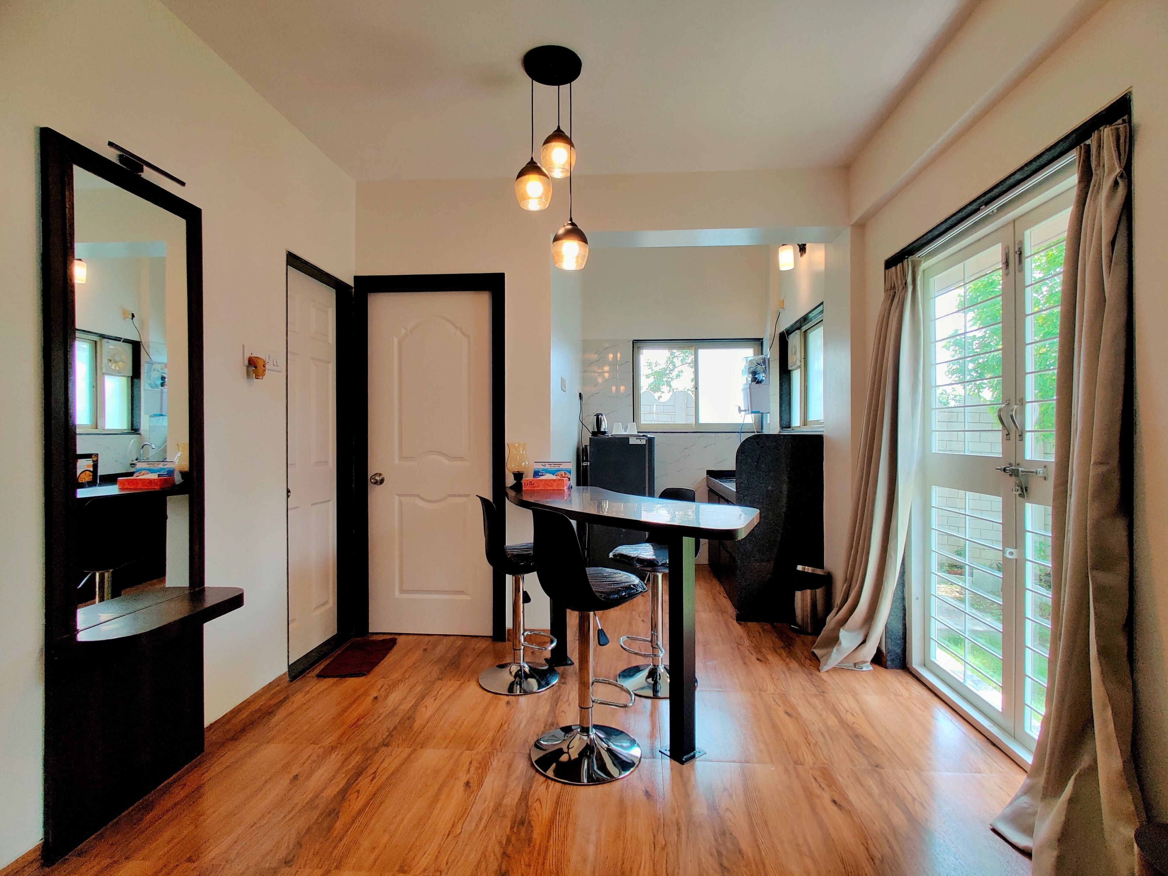 A modern kitchen with a dining area, wooden flooring, and a large window with curtains.