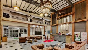 A spacious lobby with leather sofas, a reception desk, and a large TV screen. - Pushpam sanskruti Resort (Karjat)
