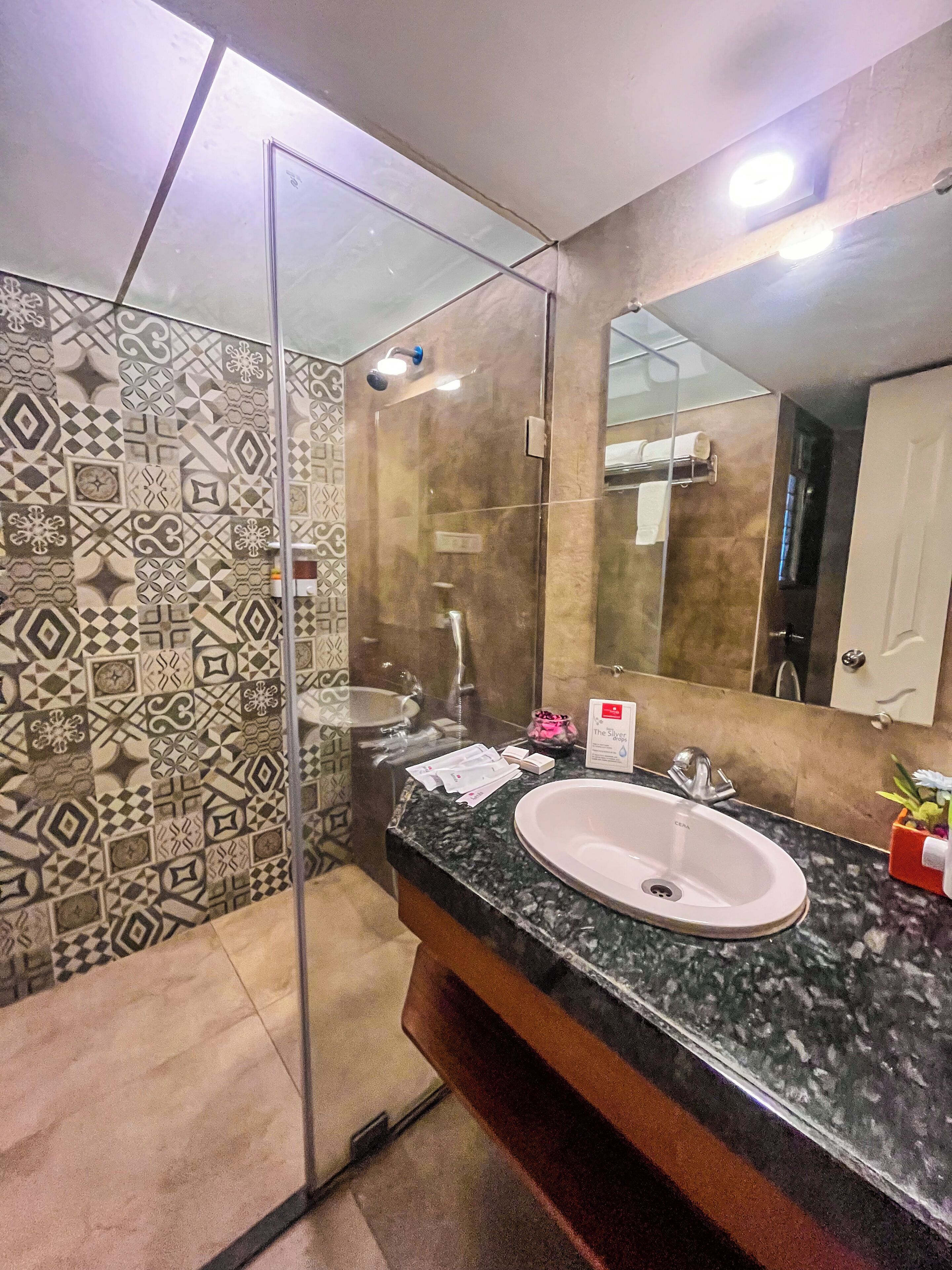 Un baño con cabina de ducha de vidrio, lavamanos con encimera de mármol y azulejos con diseño en las paredes.