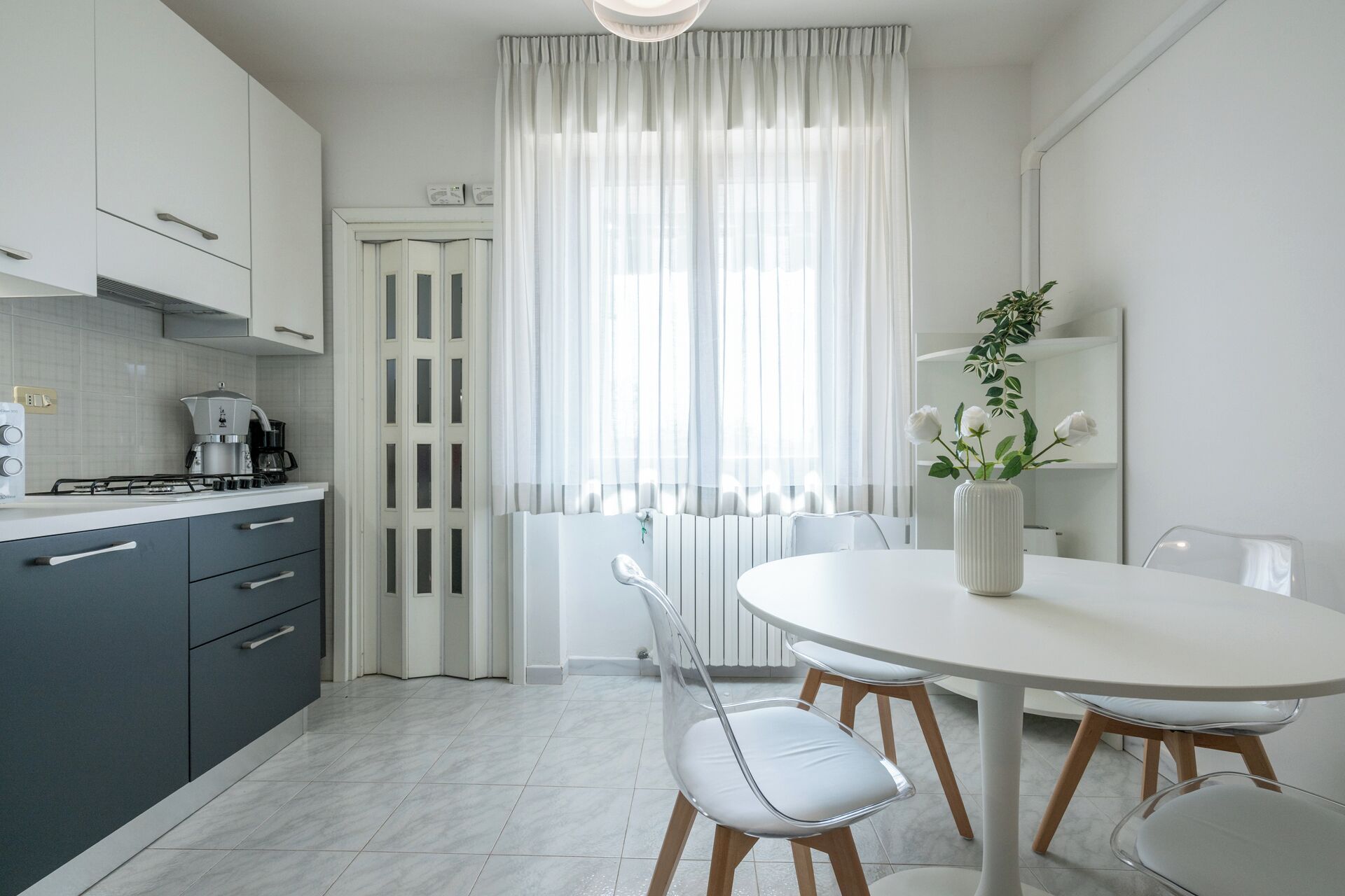Una cocina moderna con armarios blancos, una estufa a gas y un comedor con una mesa y sillas blancas.