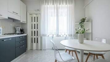 Una cocina moderna con armarios blancos, una estufa a gas y un comedor con una mesa y sillas blancas.