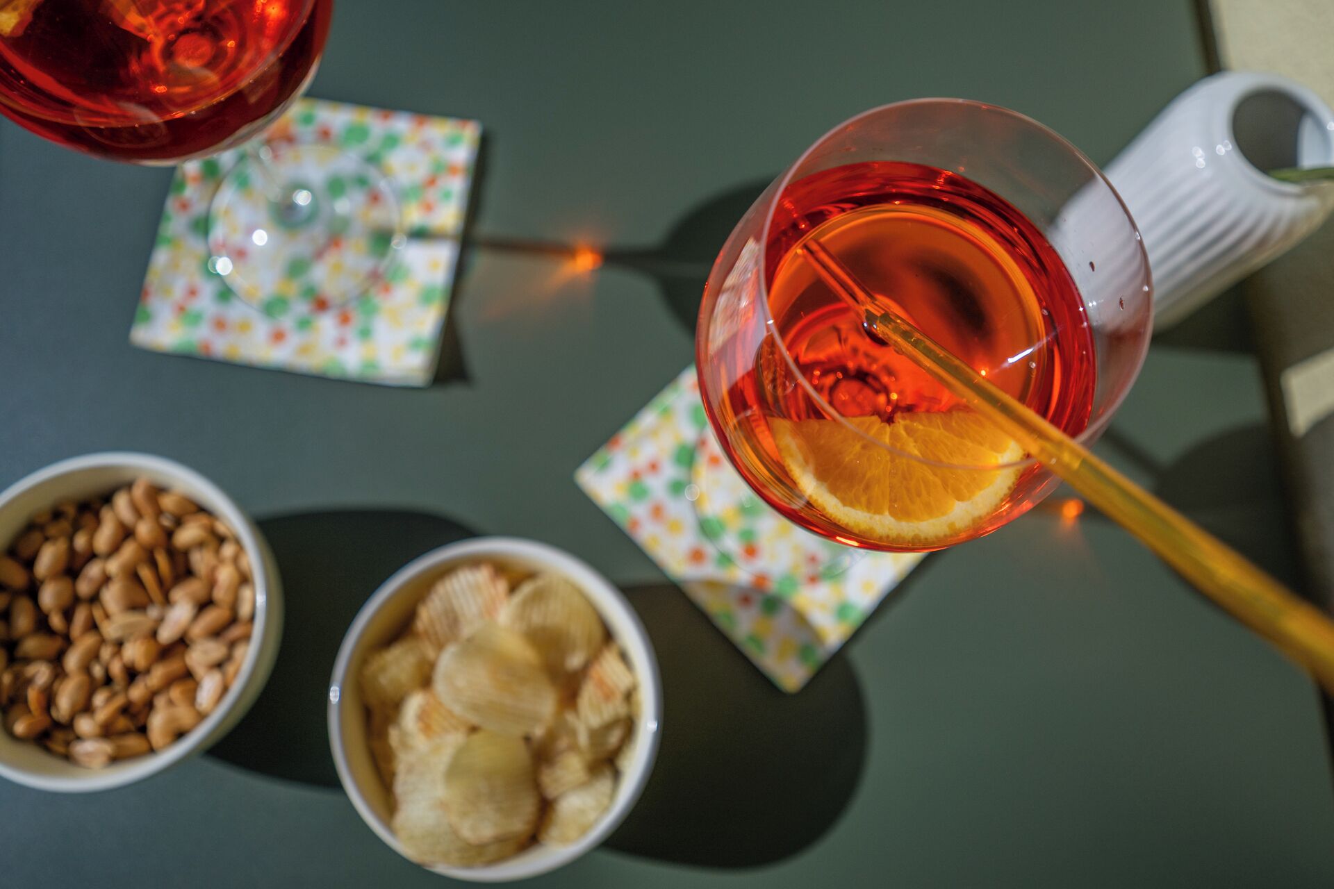 A table with a glass of tea, a white mug, and bowls of snacks.