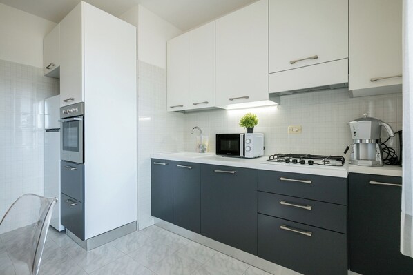 A modern kitchen with white and dark grey cabinets, a built-in oven, a microwave, a gas stove, and a coffee maker.