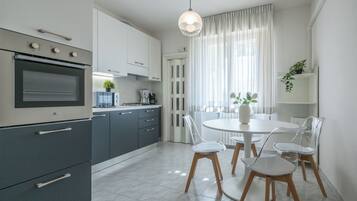 Una cocina moderna con horno empotrado, cafetera y comedor con mesa redonda y cuatro sillas.