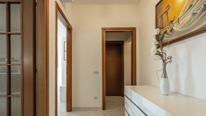 Ein Flur mit einer Holztür, einer weißen Vase mit Blumen und einem gefliesten Boden.