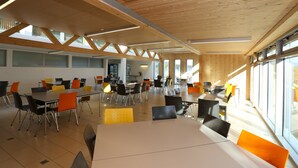 A spacious dining area with high ceilings and large windows, featuring multiple tables and chairs. - Centre St-François (Delémont)