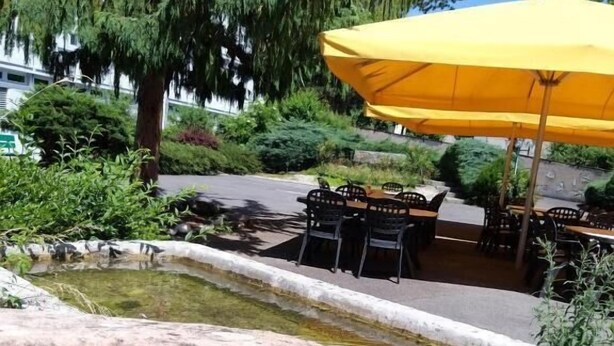 A clear outdoor pool with rocks, surrounded by greenery and outdoor seating under a yellow umbrella. - Centre St-François (Delémont)