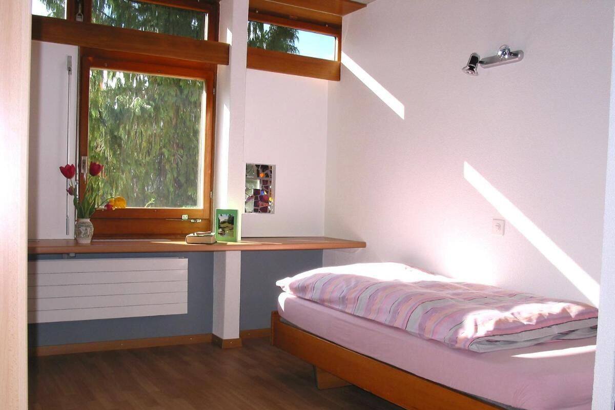 A bedroom with a wooden bed, a window with a view of trees, a bedside table with a vase, and a radiator.