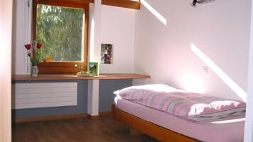 Ein Schlafzimmer mit einem hölzernen Bett, einem Fenster mit Blick auf Bäume, einem Nachttisch mit einer Vase und einem Heizkörper.