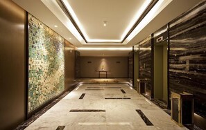 Un couloir d’hôtel avec un mur recouvert de carreaux, un sol en marbre et un ascenseur.