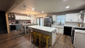 Una cocina moderna con gabinetes blancos, una isla central con taburetes, electrodomésticos de acero inoxidable y piso de madera.