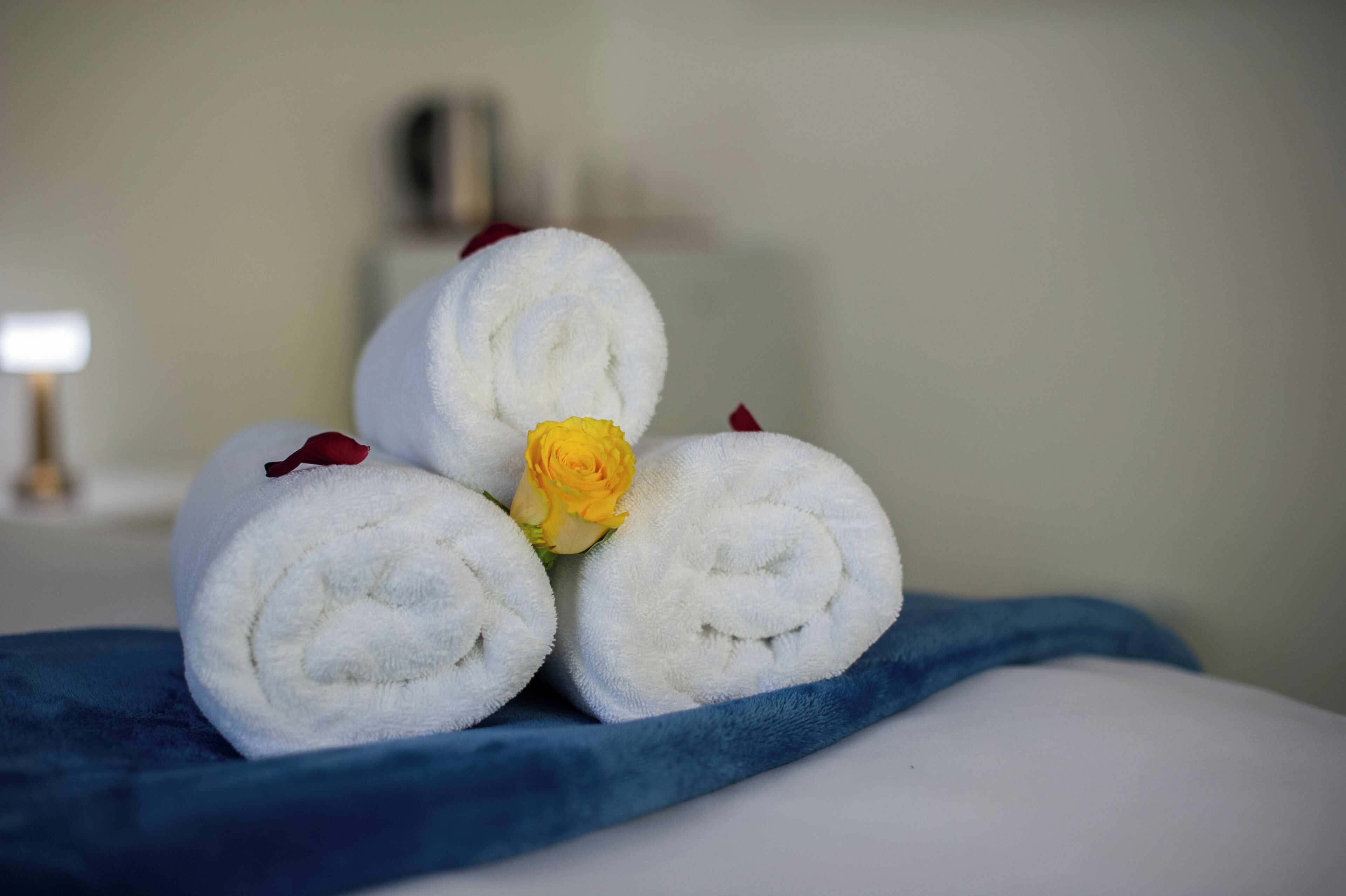 A neatly arranged set of rolled towels with a yellow rose and red petals on a blue fabric.