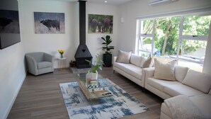 Een moderne woonkamer met een bank, fauteuil en een salontafel met een plant. Er hangen twee schilderijen aan de muur en is een open haard.