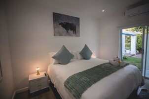 Quarto com cama, travesseiros, cobertor, mesa de cabeceira, abajur e um quadro na parede.