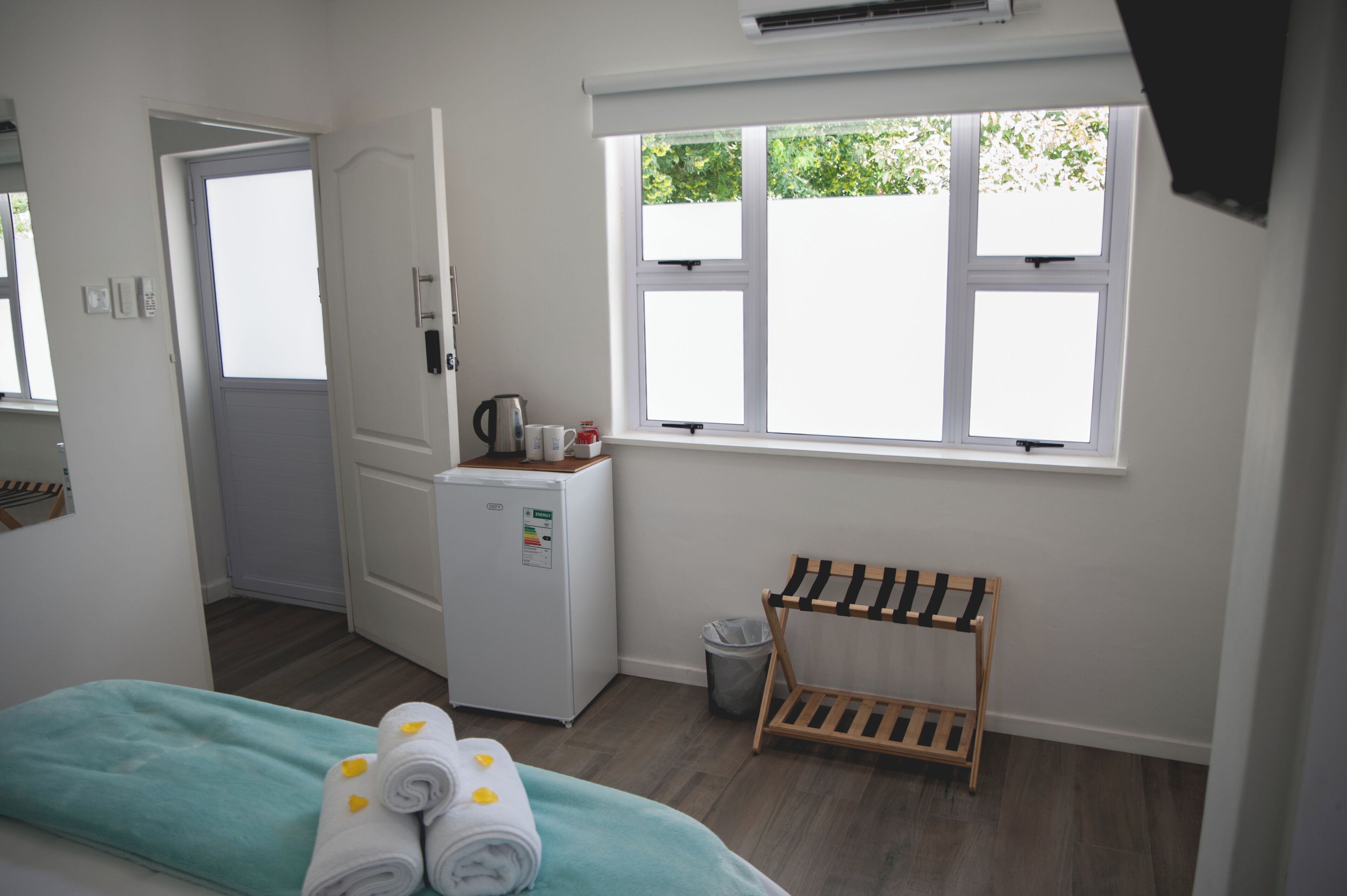 Habitación de hotel con cama, un refrigerador pequeño, ventana con vistas a la vegetación, toallero y una puerta.
