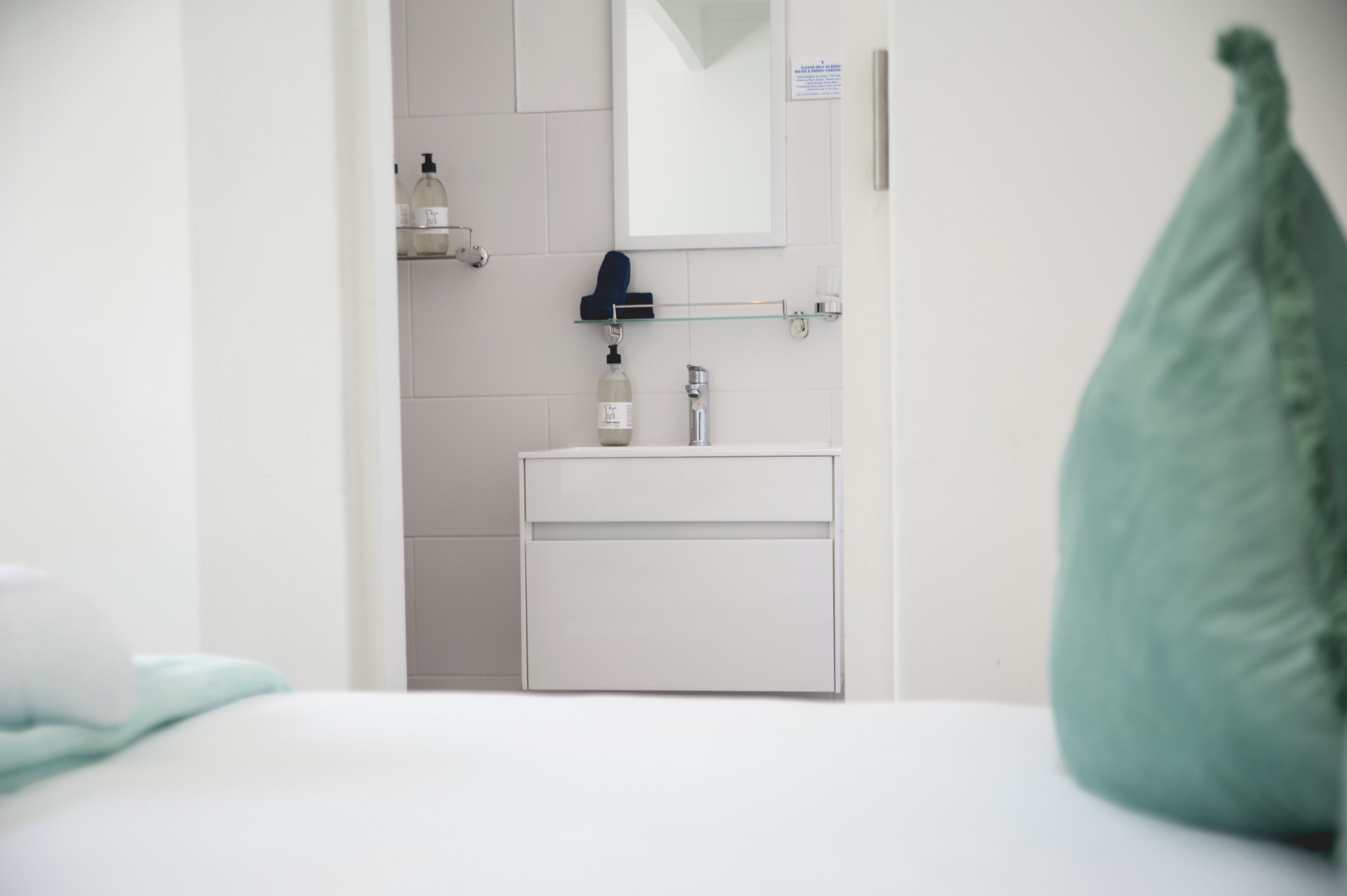 A modern bathroom with a white sink, a mirror, and a glass shelf with toiletries.