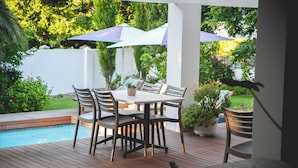 Een terras met zwembad, een tafel met stoelen en parasols.