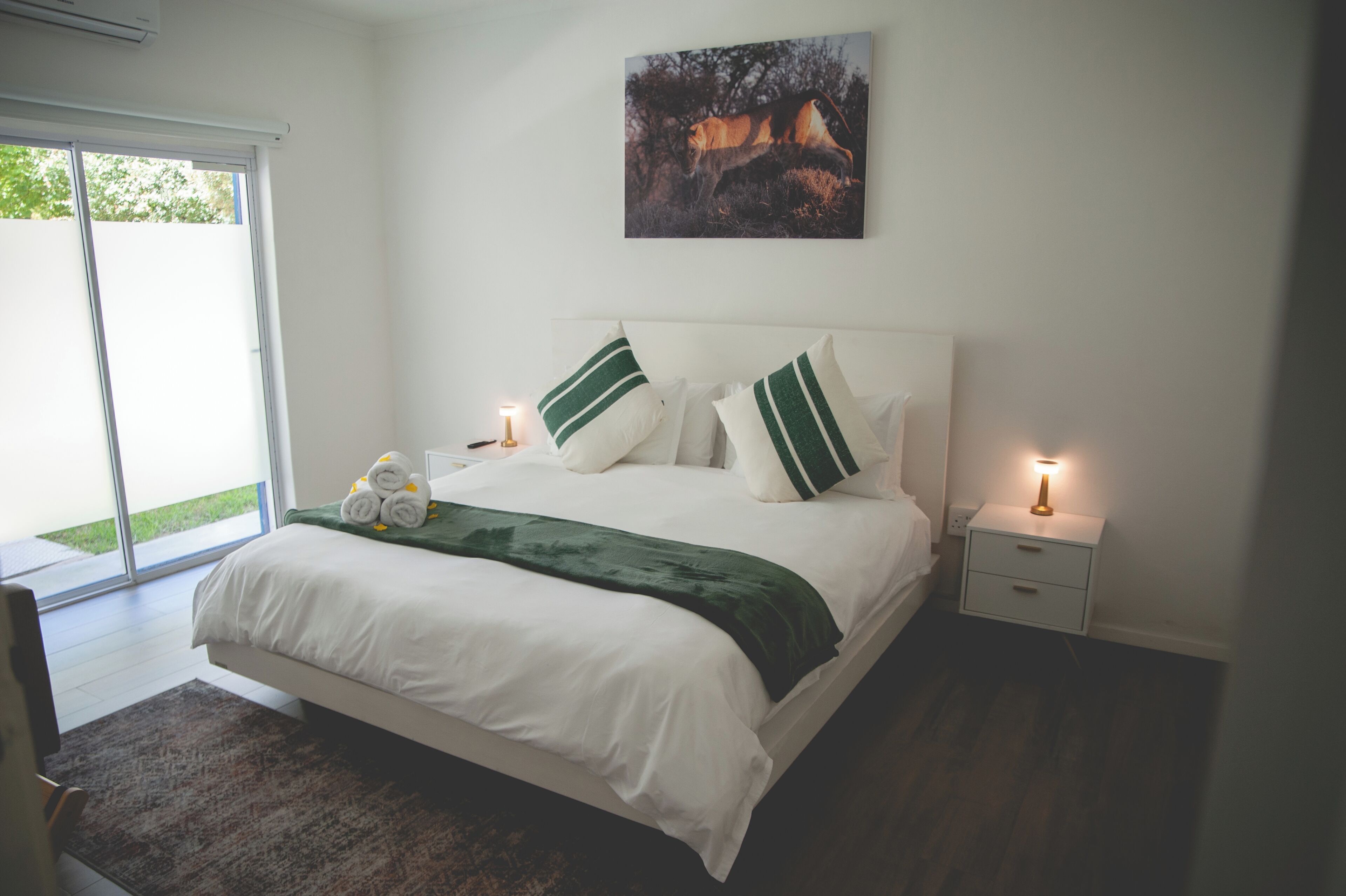 Un dormitorio con una cama, dos mesitas de noche, una lámpara de noche y un edredón verde, además de un cuadro en la pared.
