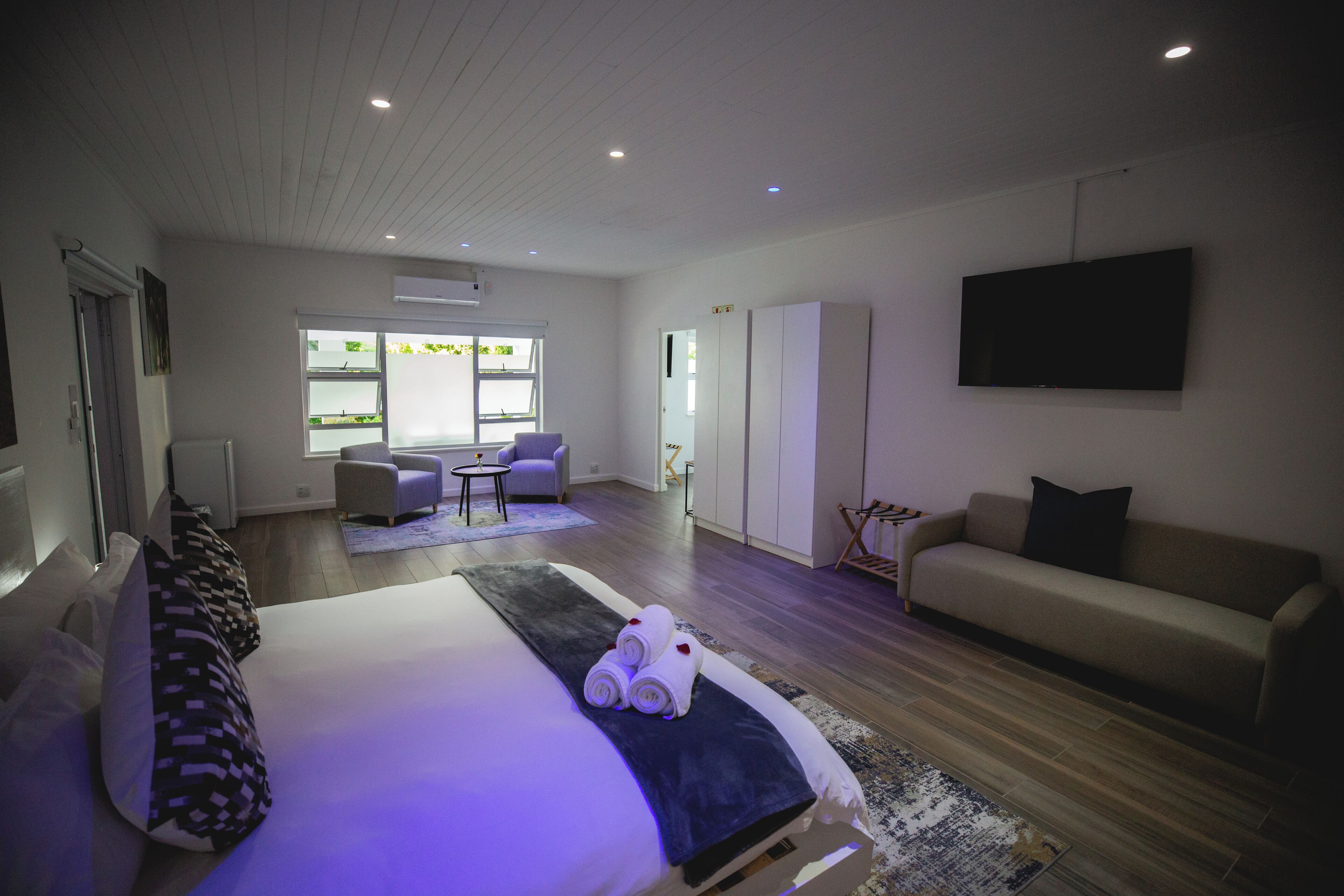 A modern hotel room with a large bed, a sofa, a TV, and a view of the outdoors through the window.