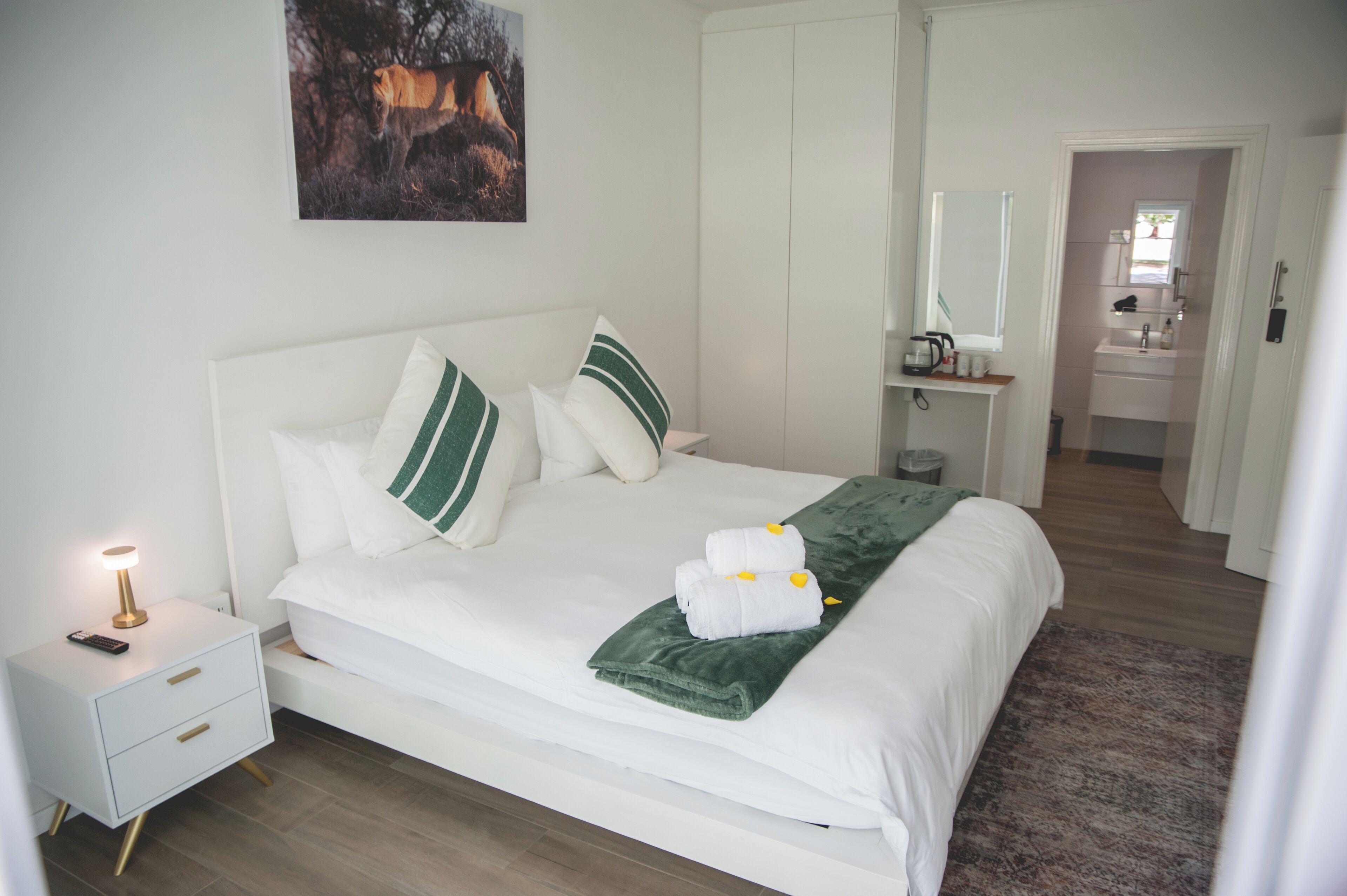 A neatly made bed with white bedding and green pillows, a bedside lamp, and a framed picture on the wall.