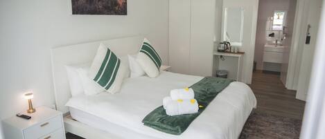 A neatly made bed with white bedding and green pillows, a bedside lamp, and a framed picture on the wall.