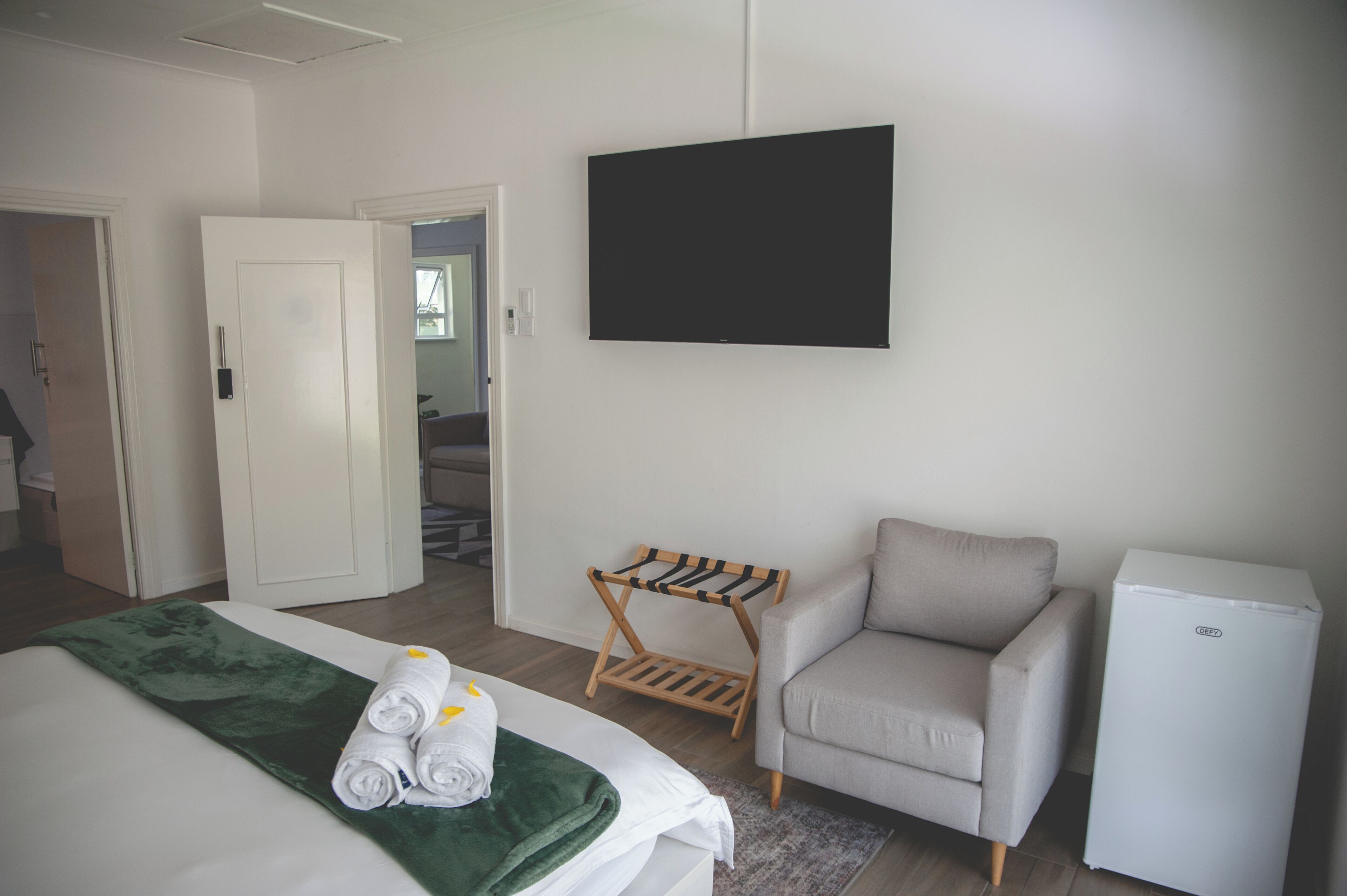 Una habitación de hotel con cama, una silla, un refrigerador pequeño y un televisor montado en la pared.