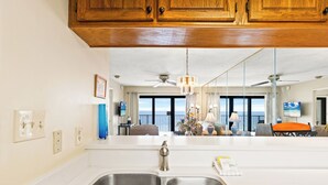 Una cocina con un lavamanos doble, armarios de madera y vistas al salón con un balcón.