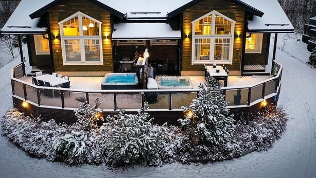 Une maison en bois à deux étages, dotée d’un patio couvert, d’un jacuzzi et surplombant un paysage enneigé.