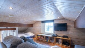 Une pièce mansardée chaleureuse avec un plafond en bois, une grande fenêtre, un téléviseur et une bibliothèque intégrée.