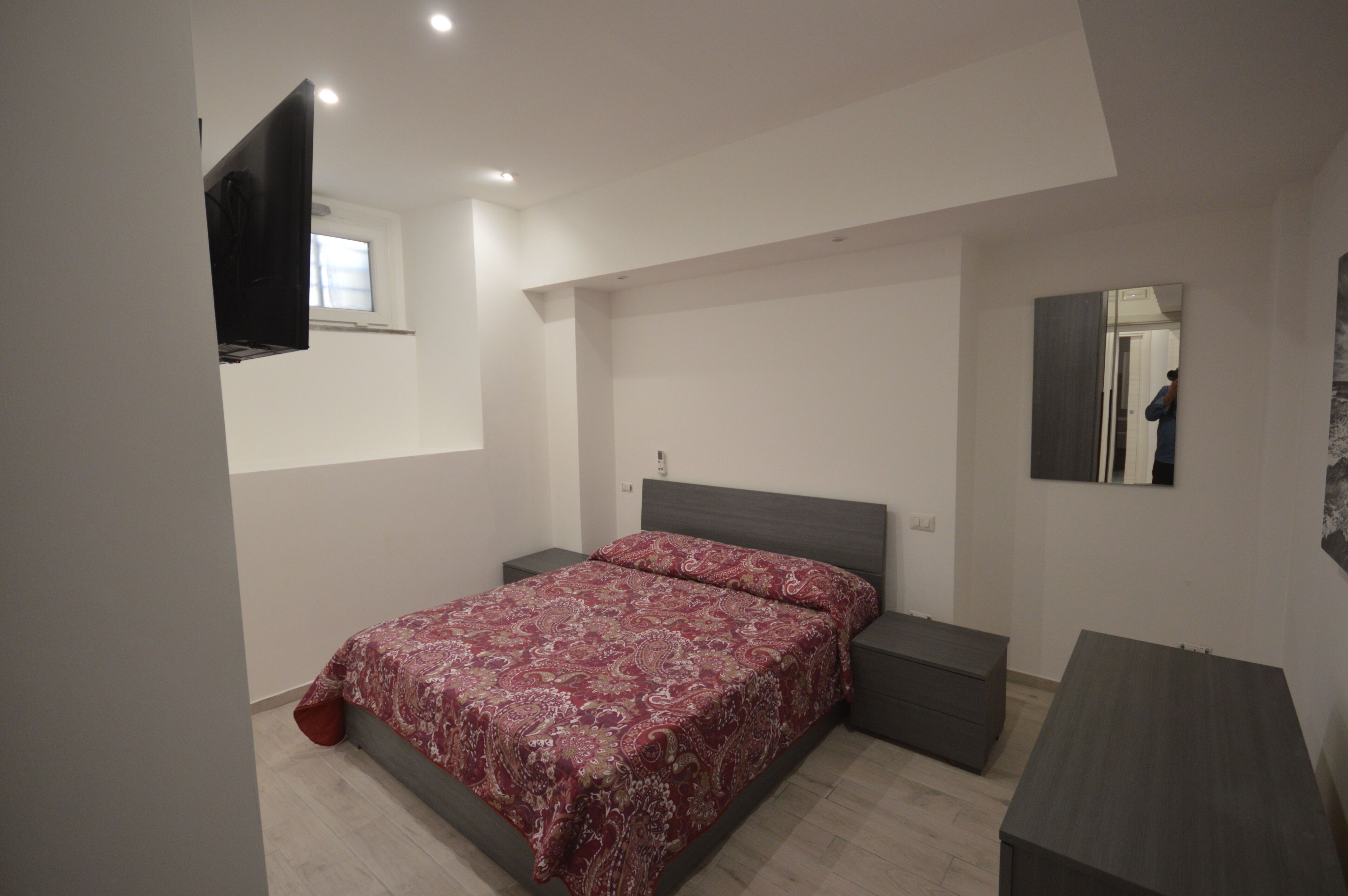 Un dormitorio con cama, mesitas de noche, televisor montado en la pared y espejo.
