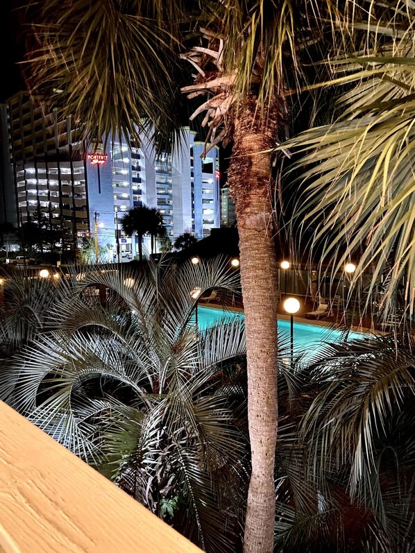 A nighttime view of a hotel with a pool surrounded by palm trees.