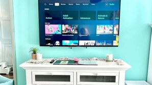 A living room with a teal wall, a white entertainment center, and a mounted TV displaying a streaming service interface.