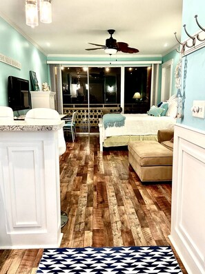 A room with a wooden floor, a bed, a sofa, a TV, and a ceiling fan.