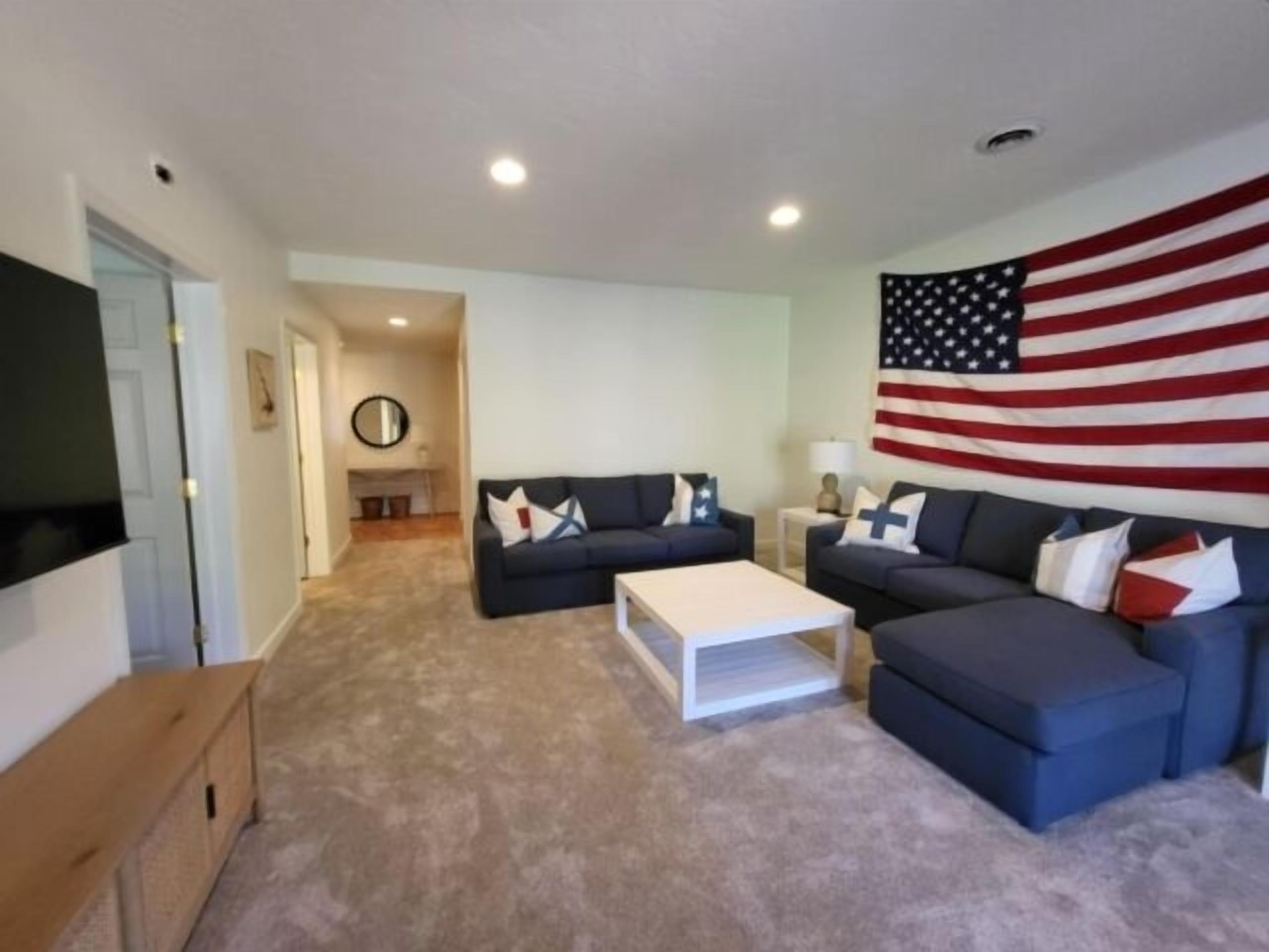 Una sala de estar con una gran bandera estadounidense, dos sofás, una mesa de centro y un televisor.