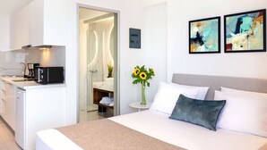 Camera d'albergo moderna con un letto, un tavolino, un forno a microonde, un lavandino e una cabina doccia. Alle pareti, due dipinti astratti.
