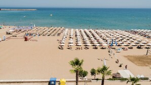 Una spiaggia con file di ombrelloni e lettini, cielo sereno e oceano sullo sfondo.