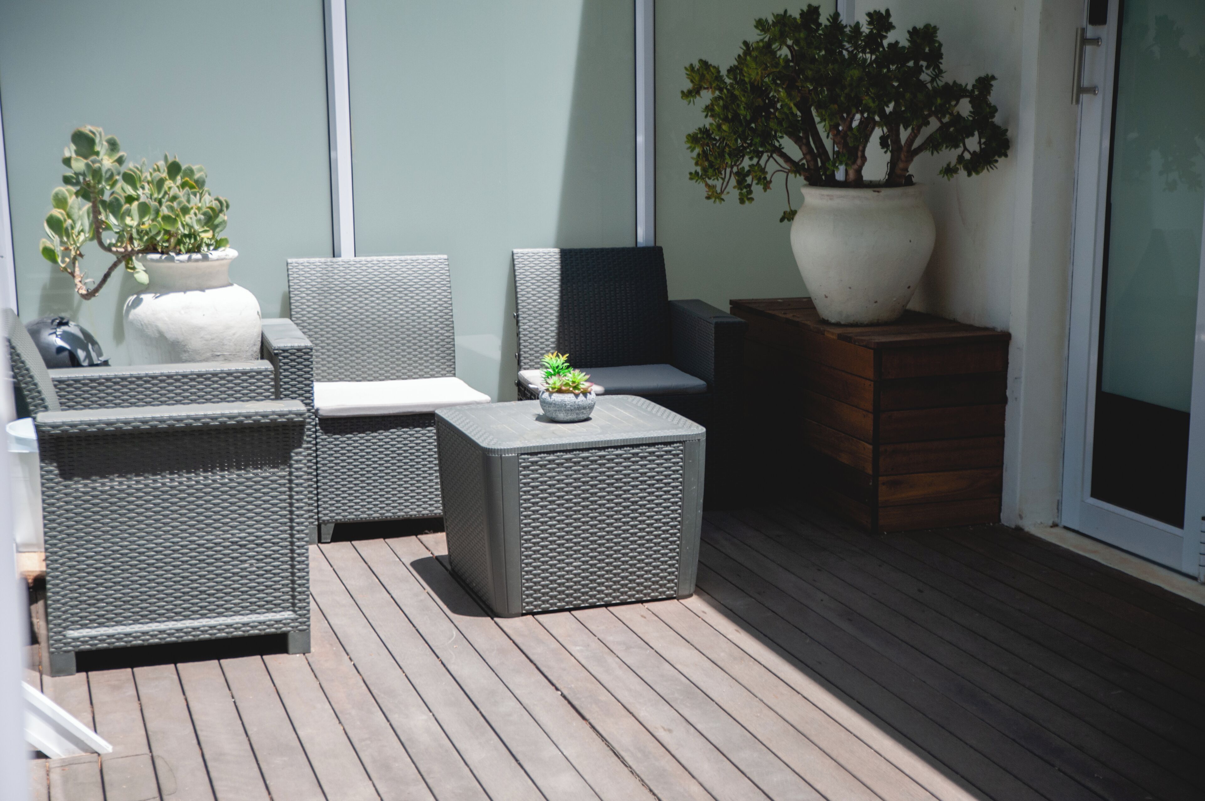A covered outdoor seating area with wicker furniture, potted plants, and a wooden bench.