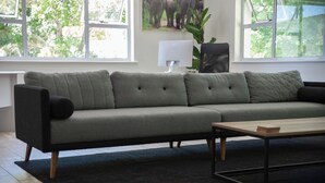 Een moderne woonkamer met een grijze modulaire bank, een houten salontafel en een zwart tapijt.