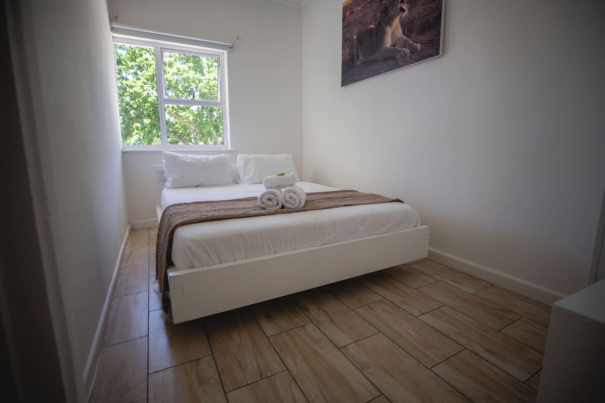 A bedroom with a bed, white bedding, a window, and a painting on the wall.