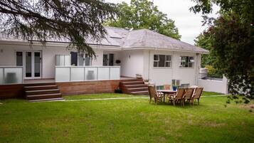 A modern house with a covered patio, a lawn, and a dining area with outdoor furniture.