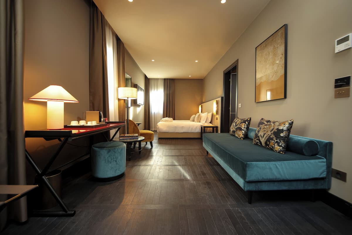 Een moderne hotelkamer met een bed, een blauwe bank, een bureau met een lamp en een televisie.