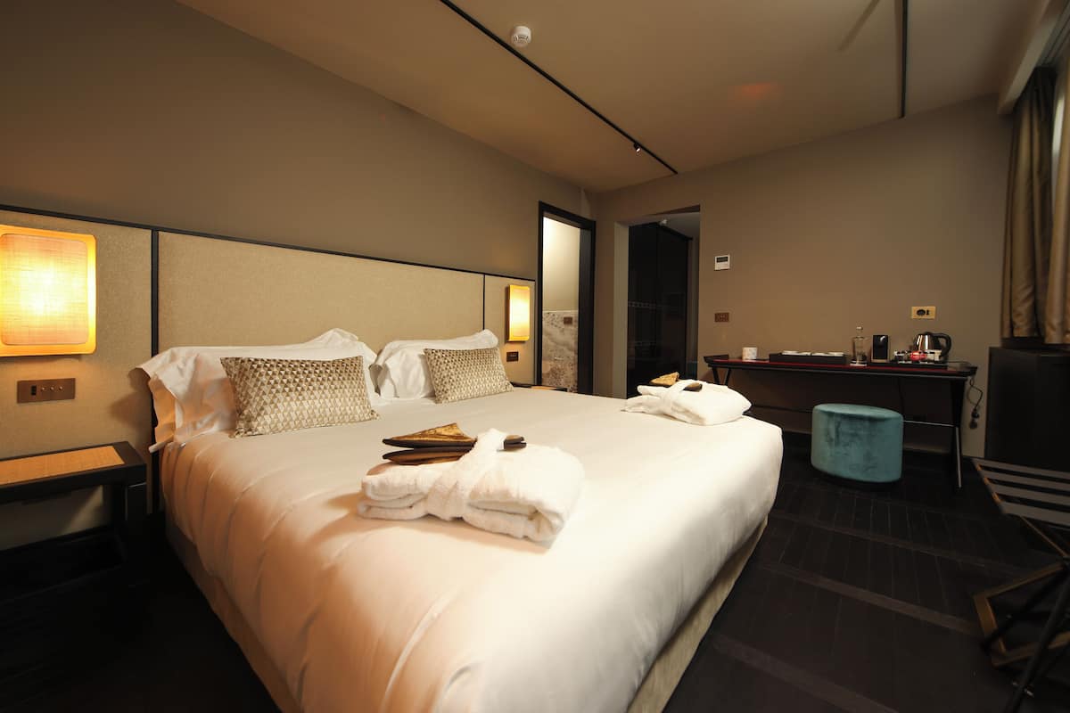 Een hotelkamer met een groot bed, een bureau met een computer, en een badkamer zichtbaar door een open deur.