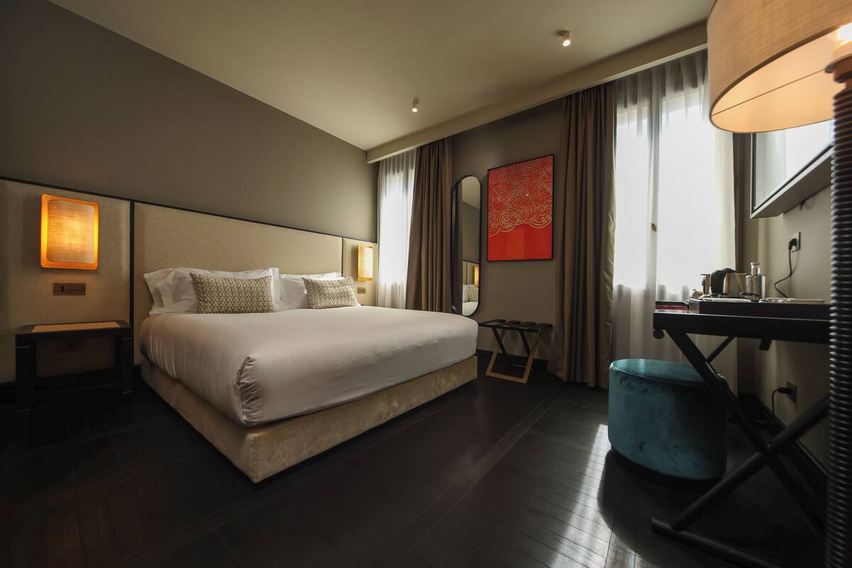 Een moderne hotelkamer met een groot bed, nachtkastjes, een bureau en een spiegel.