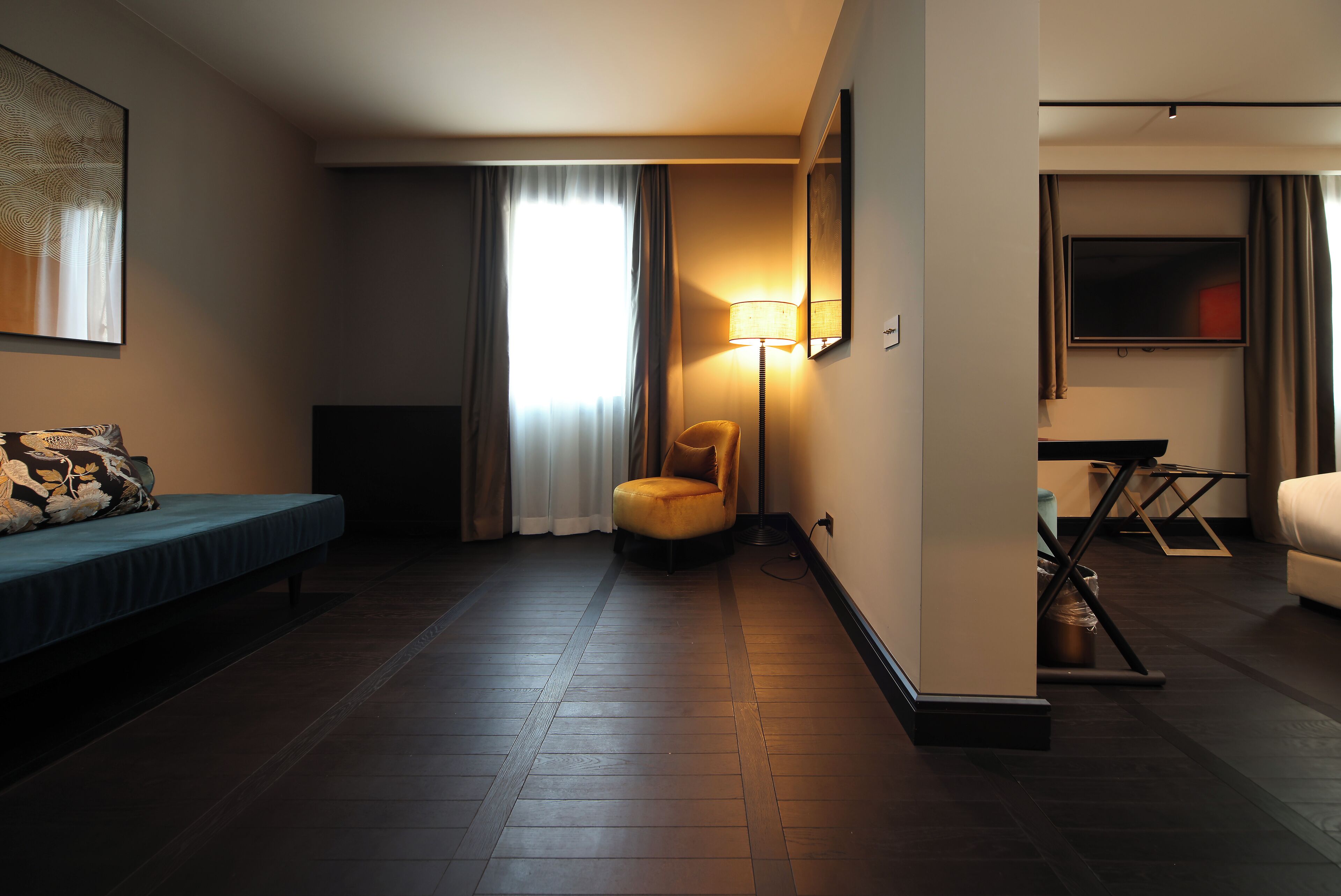 A hotel room with a bed, a chair, a lamp, a TV, and a small table.