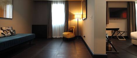 A hotel room with a bed, a chair, a lamp, a TV, and a small table.