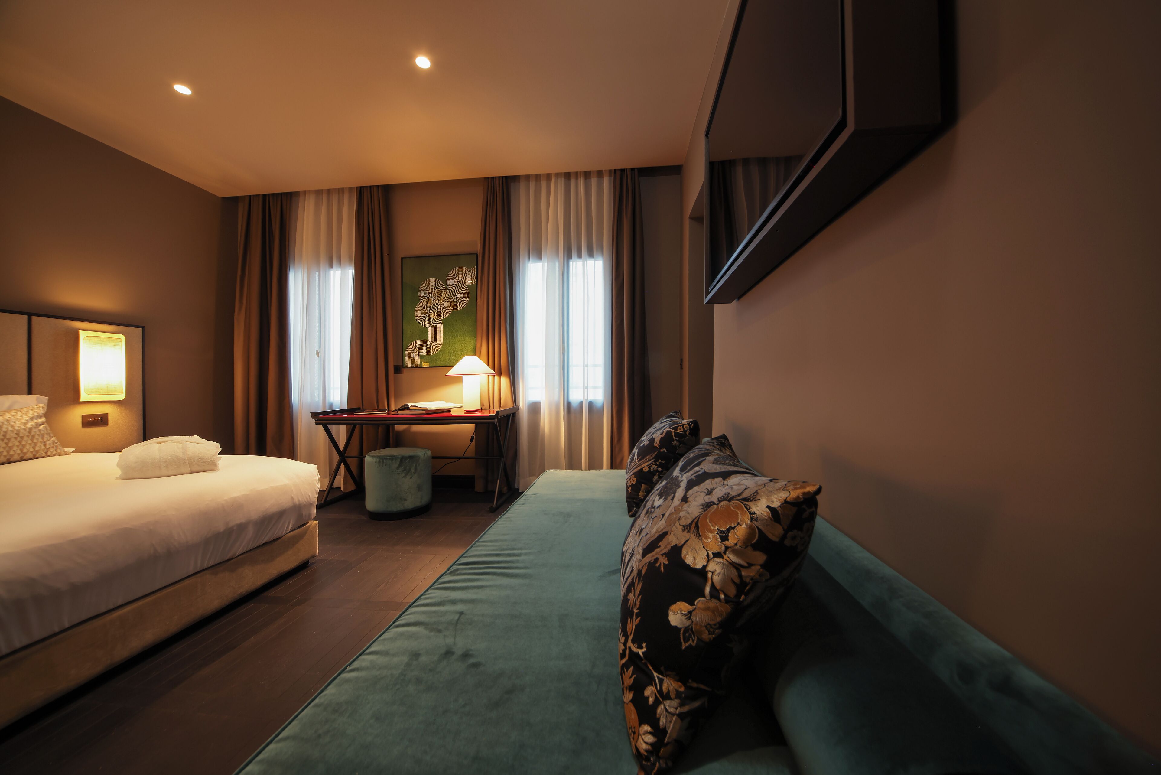Una habitación de hotel con cama, sofá, escritorio con lámpara y un cuadro en la pared.