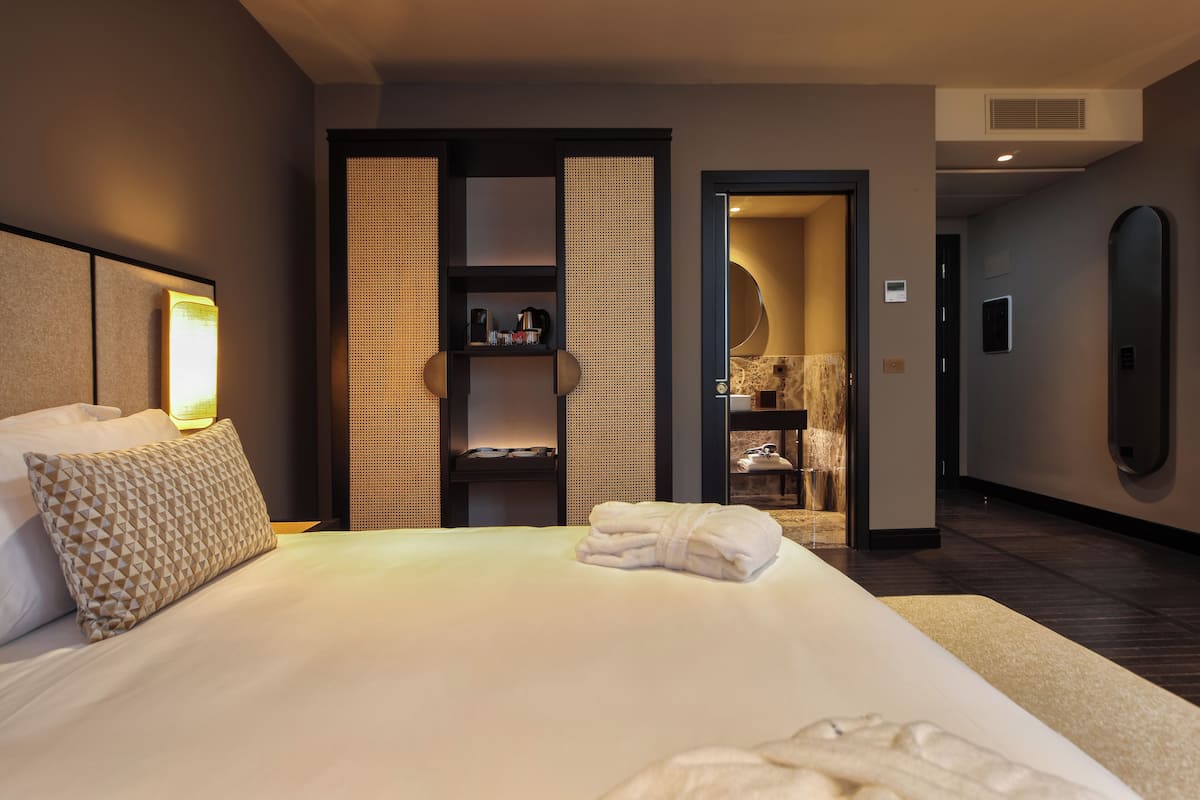 Een hotelkamer met een groot bed, een nachtkastje, een kledingkast en een badkamer die door een geopende deur zichtbaar is.